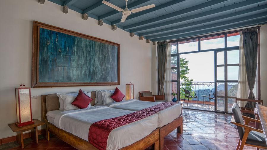 Bedroom featuring a king-size bed with red accents, large artwork, wooden furniture, and a balcony with a scenic view. | Mango Hill, Yercaud