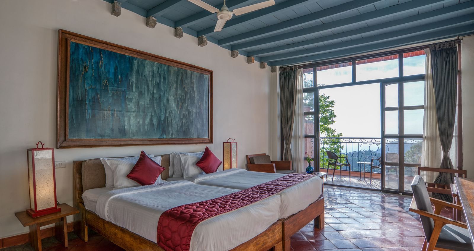 Bedroom featuring a king-size bed with red accents, large artwork, wooden furniture, and a balcony with a scenic view. | Mango Hill, Yercaud