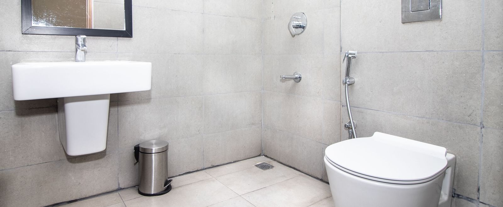 A bathroom with a white toilet, sink, shower fitting, and tiled walls and floor - Sanctum Suites Richmond Road, Bangalore