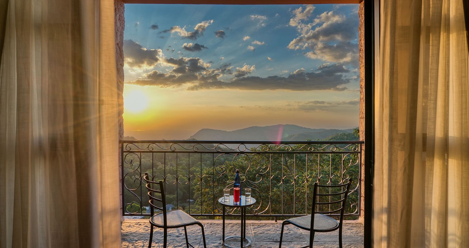 Sunset view from a balcony with two chairs and a table, overlooking green valleys and mountains.  | Mango Hill, Yercaud