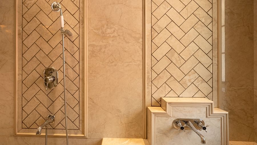 Luxurious beige marble shower area with chrome fixtures, featuring an elegant herringbone tile pattern on recessed wall panels - Panna Vilas Palace