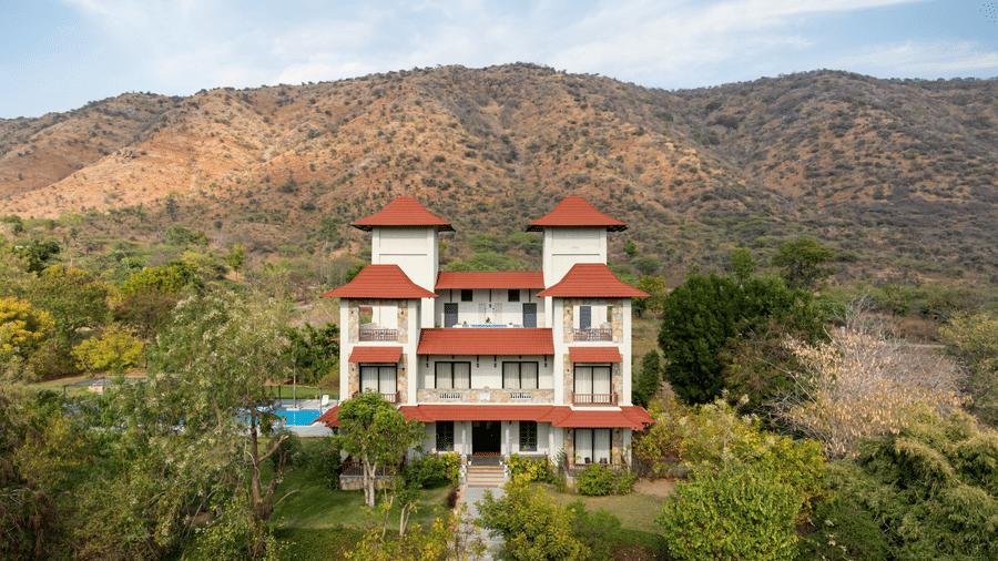 A wide-angle shot of the exterior of The Hunting Lodge, Udaipur, nestled amid the jungle the hills of the Aravallis in the background.
