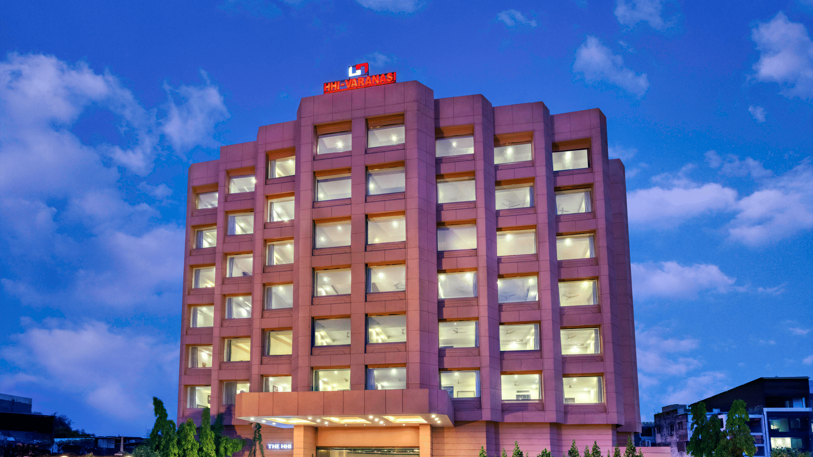 A multi-storey brown building with illuminated windows under a blue sky at dusk | HHI Varanasi