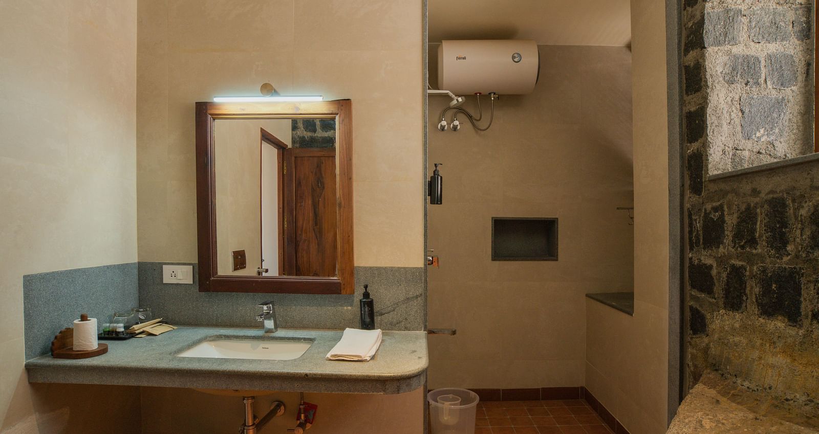 A modern bathroom with minimalist design, featuring a large mirror, simple fixtures, and a stone accent wall.  | Mango Hill, Yercaud