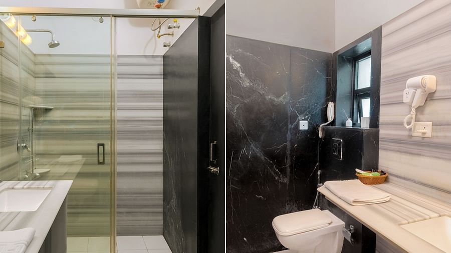 A spacious bathroom with a wall-mounted mirror above the washbasin, a western toilet on the side, and a glass partition dividing the shower area | Panna Vilas Udaipur