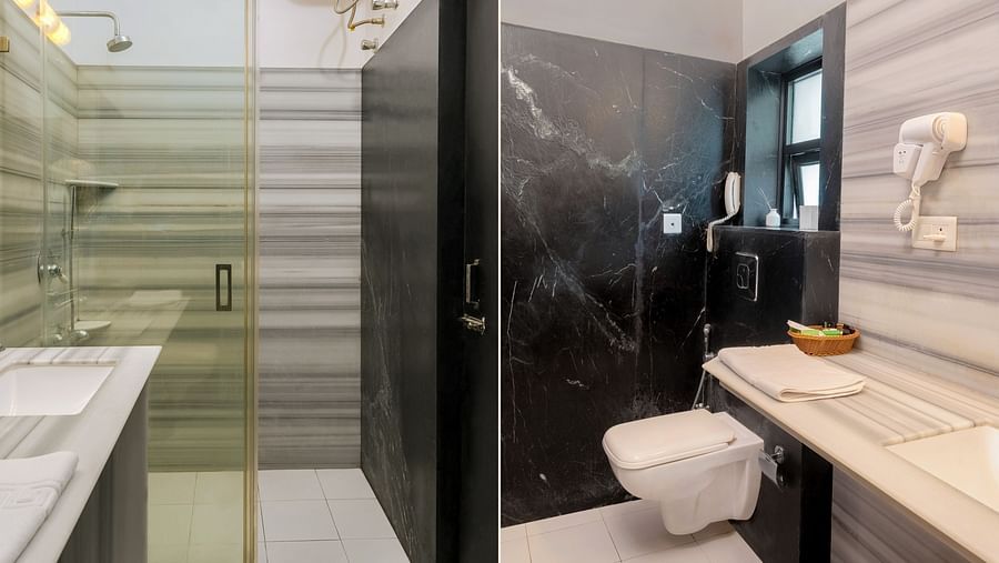 A spacious bathroom with a wall-mounted mirror above the washbasin, a western toilet on the side, and a glass partition dividing the shower area | Panna Vilas Udaipur
