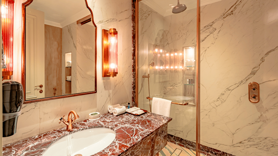 A shower cubicle separated by a glass partition at the bathroom of Royal Club Room, along with a neatly kept vanity area at Noor-Us-Sabah Palace, Bhopal.