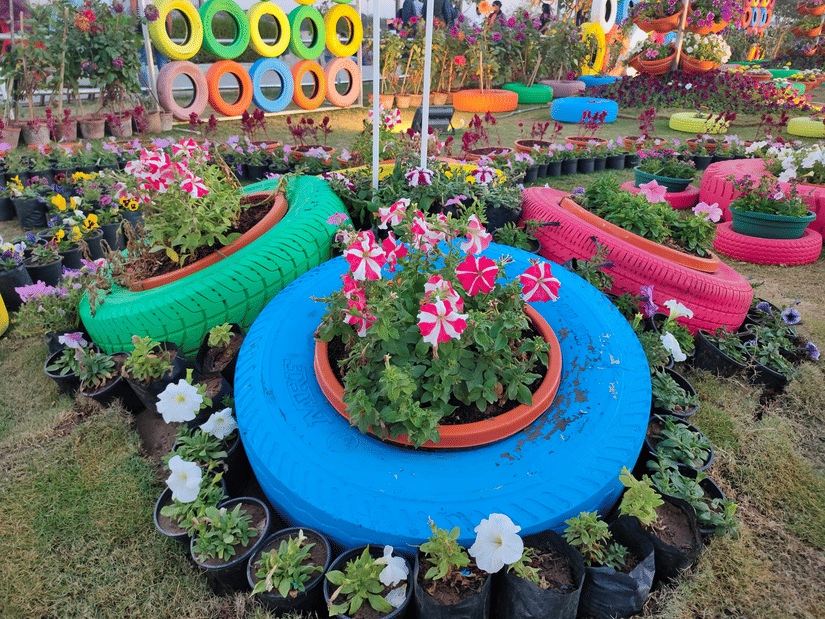 A vibrant garden display features colourful painted recycled tyres used as planters for flowers and plants.