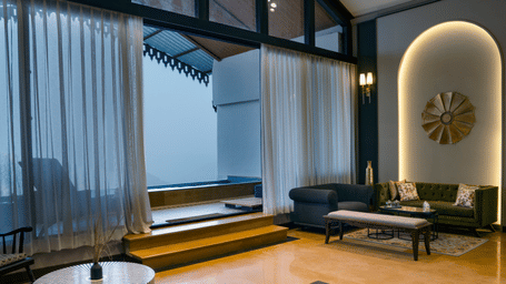 Presidential Suite living area at Polo Resort Cherrapunji with sheer curtains, green velvet sofa, arched niche with sunburst wall art and a sunken plunge pool.