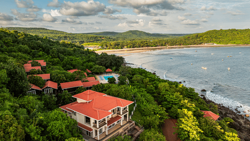 An image showcasing a resort by the side of the sea covered in lush green trees on all sides - Highland Sarovar Portico, Sindhudurg