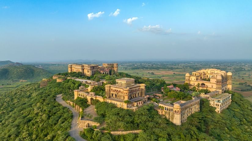 An aerial view of Tijara Fort-Palace atop a lush green hill, showcasing the fort's architecture and the surrounding landscape under a clear blue sky - Tijara Fort-Palace - 19th Century, Alwar.