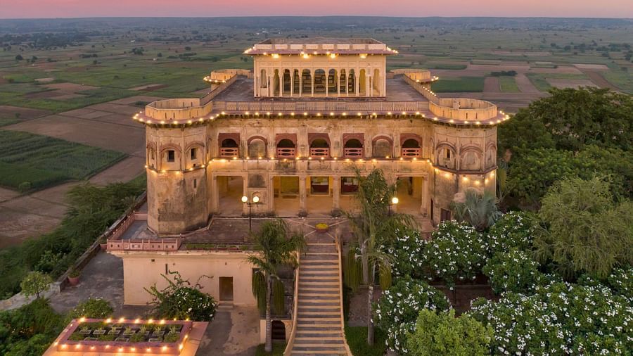 Facade image of Tijara Fort-Palace - 19th Century, Alwar surrounded by lush greenery with orange hued sky in the background - Hotel in Tijara