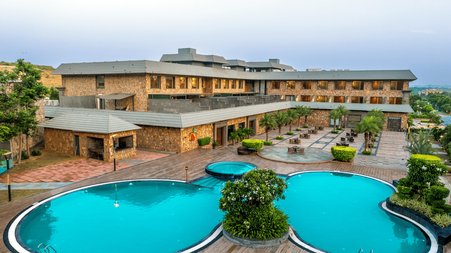 An aerial shot of the swimming pool surrounded by a wooden deck overlooking the resort building - Pushkara Resort & Spa, Ajmer