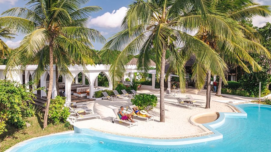 View of a swimming pool and a man and a woman with palm trees and buildings in the background - Shooting Star Boutique Hotel.