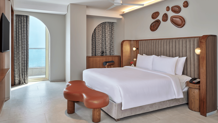 The Intimate Escape Suite at Swosti Premium Beach Resorts, Puri, with a double bed, cushion, wooden wall art, and  a large window. 