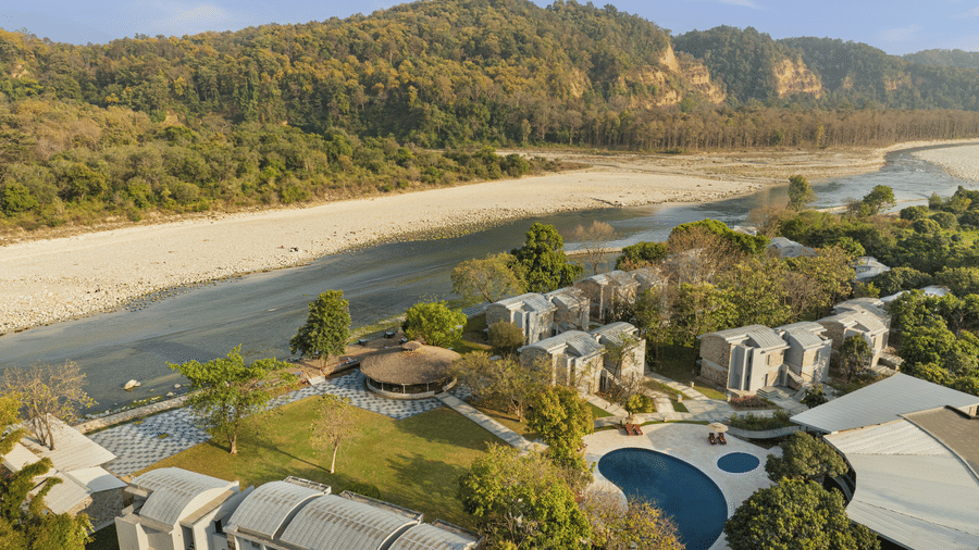 Scenic aerial view of resort buildings, swimming pool, and forested hills near the river at The Corbett Hideaway.
