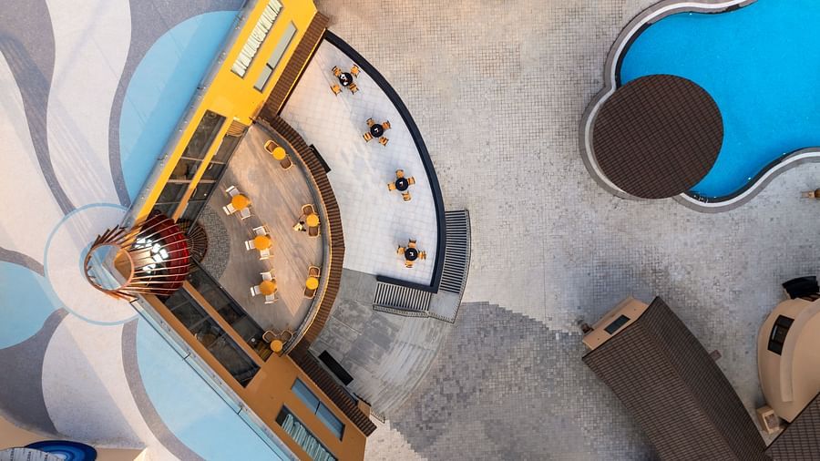 An aerial view of The Qualia Resort Club & Brewery, Udaipur capturing a uniquely designed pool area with geometric shapes and surrounding landscaping.
