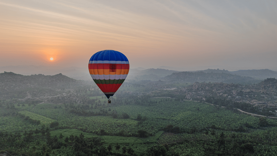 Hot air balloon floating over green Hampi valley at sunrise near Evolve Back resort
