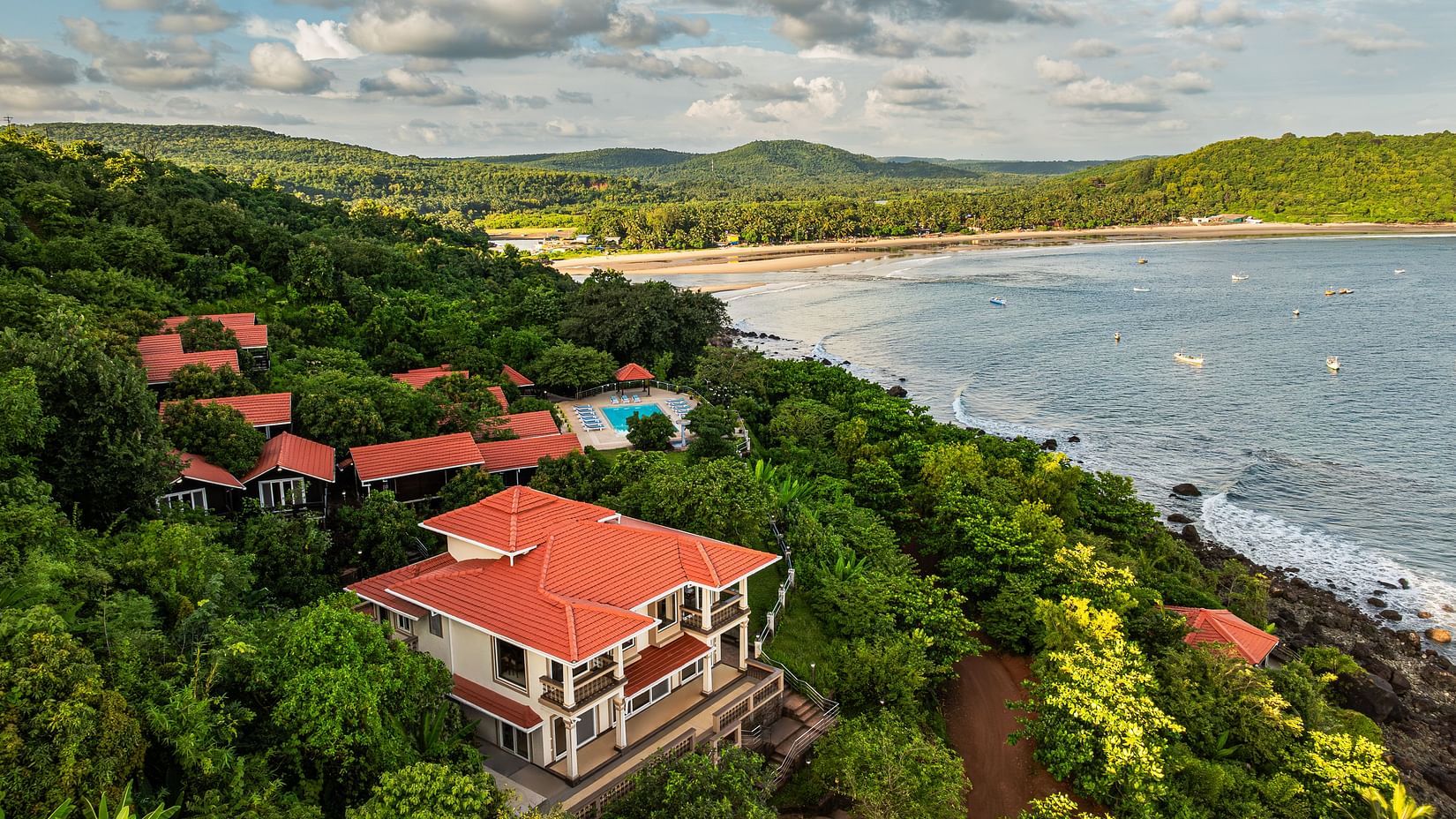 An image showcasing a resort by the side of the sea covered in lush green trees on all sides - Highland Sarovar Portico, Sindhudurg