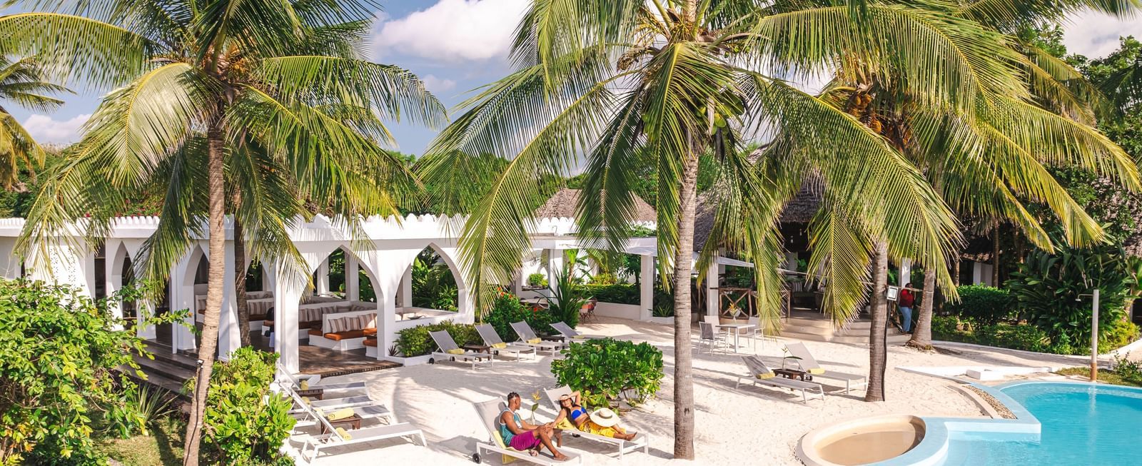 View of a swimming pool and a man and a woman with palm trees and buildings in the background - Shooting Star Boutique Hotel.