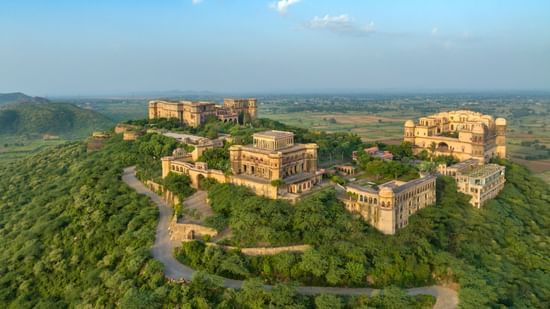 Tijara Fort Palace set amidst the lush green plants and trees spread far across. There's also a road leading to the fort.