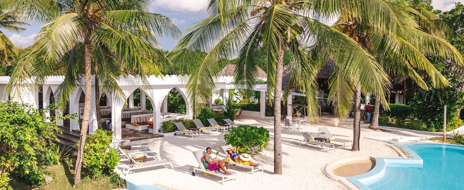 View of a swimming pool and a man and a woman with palm trees and buildings in the background - Shooting Star Boutique Hotel.