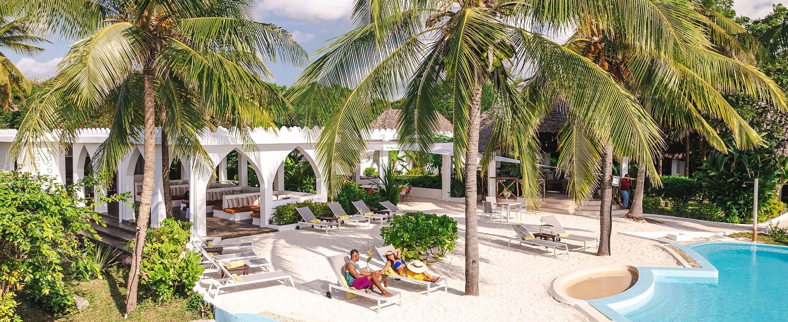 View of a swimming pool and a man and a woman with palm trees and buildings in the background - Shooting Star Boutique Hotel.