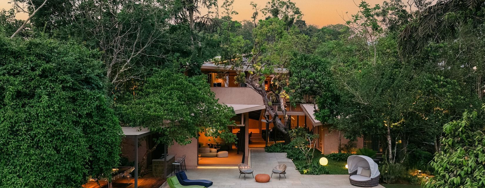 An evening view of Villa Moira by V Escapes, highlighting the illuminated swimming pool and outdoor lounge areas amidst the twilight glow.
