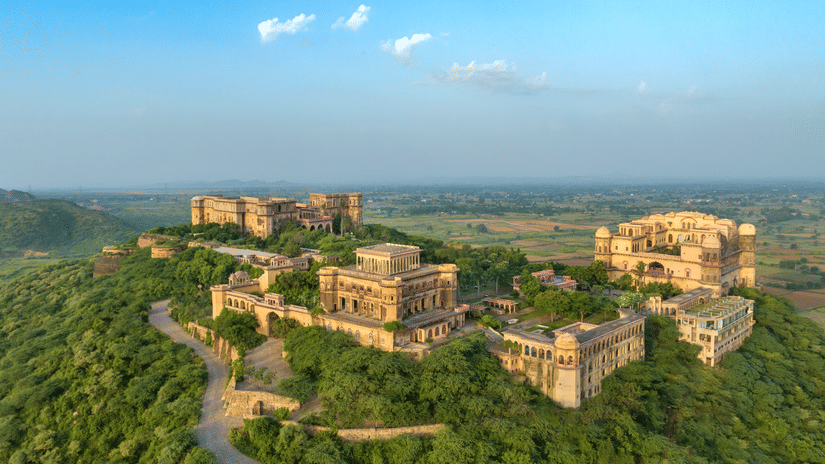 Tijara Fort Palace set amidst the lush green plants and trees spread far across. There's also a road leading to the fort.