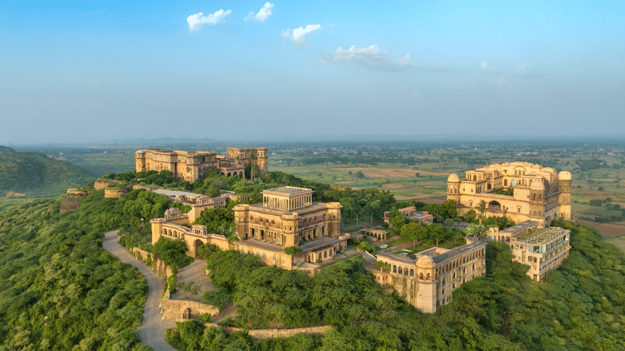 Tijara Fort Palace set amidst the lush green plants and trees spread far across. There's also a road leading to the fort.