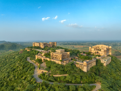 An aerial view of Tijara Fort-Palace atop a lush green hill, showcasing the fort's architecture and the surrounding landscape under a clear blue sky - Tijara Fort-Palace - 19th Century, Alwar.