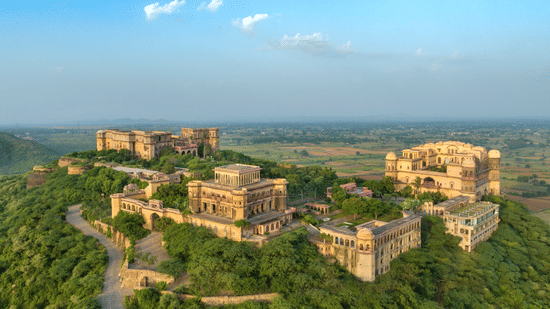Tijara Fort Palace set amidst the lush green plants and trees spread far across. There's also a road leading to the fort.