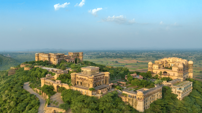 An aerial view of Tijara Fort-Palace atop a lush green hill, showcasing the fort's architecture and the surrounding landscape under a clear blue sky - Tijara Fort-Palace - 19th Century, Alwar.
