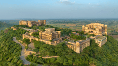 An aerial view of Tijara Fort-Palace atop a lush green hill, showcasing the fort's architecture and the surrounding landscape under a clear blue sky