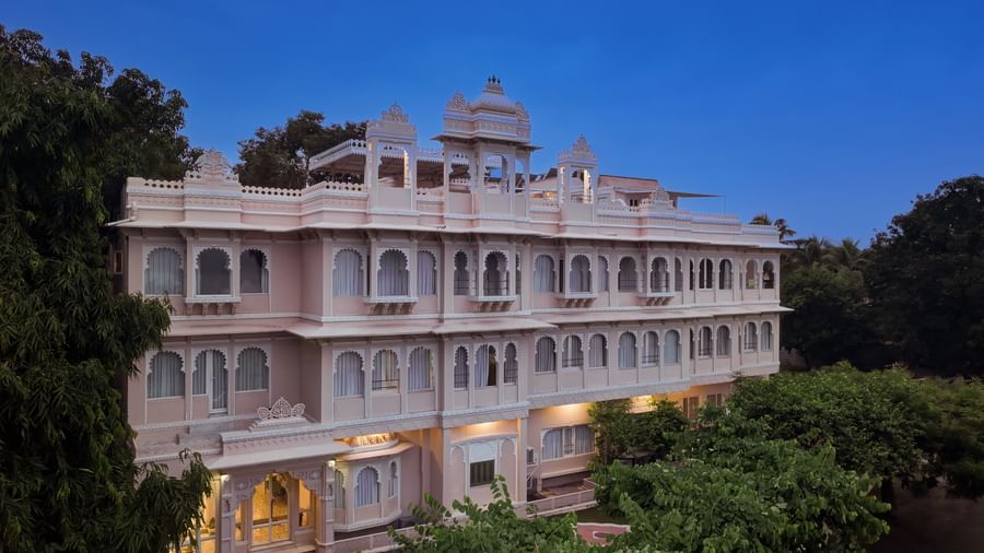 Exterior of Ram Pratap Palace at dusk, showcasing the three-story building with traditional arched windows, ornate balconies, and a lit entrance.