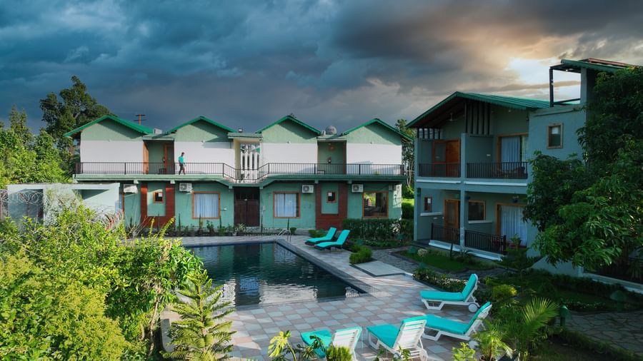 A resort with a beautiful outdoor swimming pool and modern villas under a dramatic, cloudy sky at Corbett Nirvana Resort.