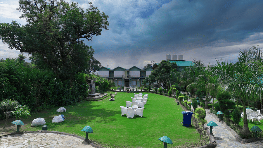 Lawn 2 with white chairs arranged on it alongside a bricked pathway lined with exterior lights at Corbett Nirvana Resort.