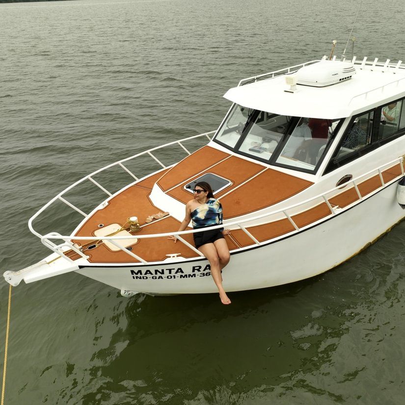 A low-angle shot of a white and brown motorboat with a woman sitting in the front cabin, moored on a murky body of water.