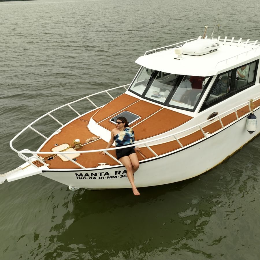 A low-angle shot of a white and brown motorboat with a woman sitting in the front cabin, moored on a murky body of water.