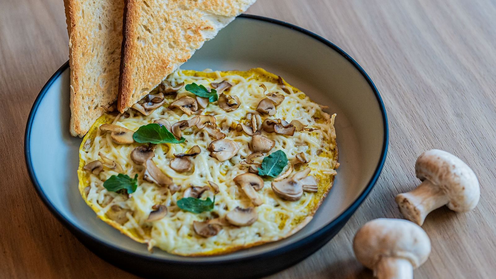 A deep plate with mushroom omelette, basil leaves, toast on the side, and mushrooms beside the plate at Indie Stays Mumbai International Airport.