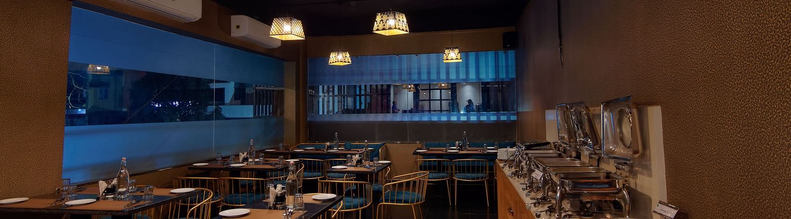 Interior of M Cafe with chairs and tables and lights hanging from the ceiling at Ankit Hotel, Jabalpur