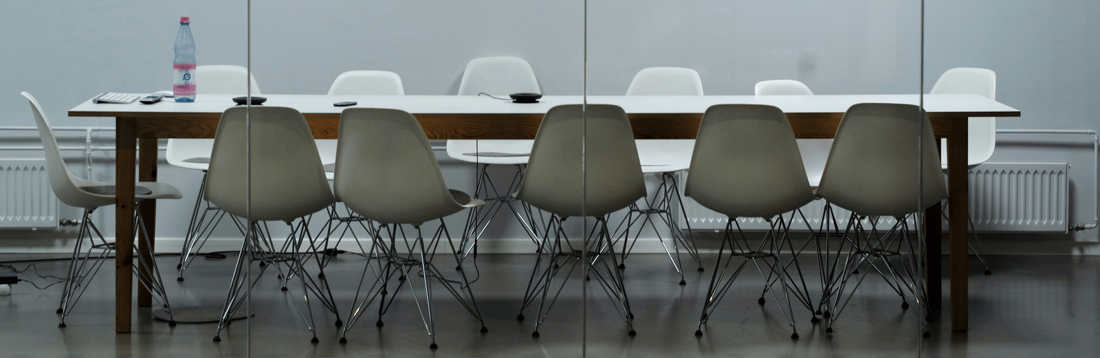 A conference room with a long wooden table, several chairs, and a glass wall in the background.