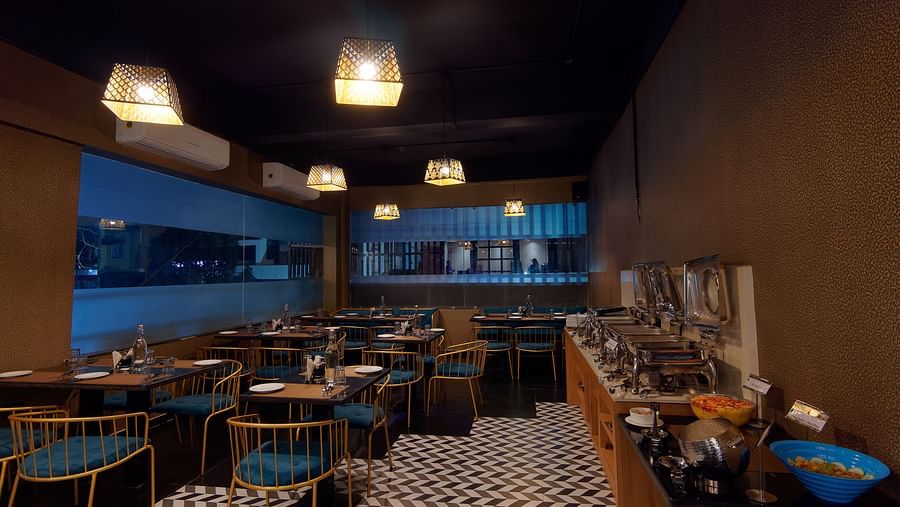 Interior of M Cafe with chairs and tables and lights hanging from the ceiling at Ankit Hotel, Jabalpur