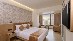 A well-lit room with a king size bed, wall-mounted TV, seating area, and stylish interior decor at Biznotel by Pride Motera, Ahmedabad.