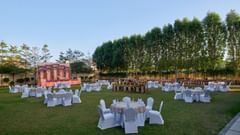 An outdoor lawn with tables and chairs with trees on the side at Tulip Inn, Bhopal.