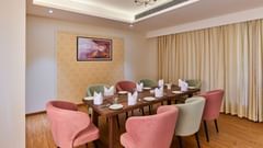 An image of a restaurant at Tulip Inn, Bhopal, showcasing a rectangular table surrounded by chairs and adorned with a chandelier overhead.