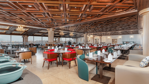An image of our restaurant in Srinagar with high ceilings made of wooden ascents and spacious dining arrangement - Sarovar Premiere, Srinagar 