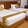 Twin bed room at Featherlite Evoma Hotel with beds dressed in white and gold linen, wooden headboards and long curtains by the window.