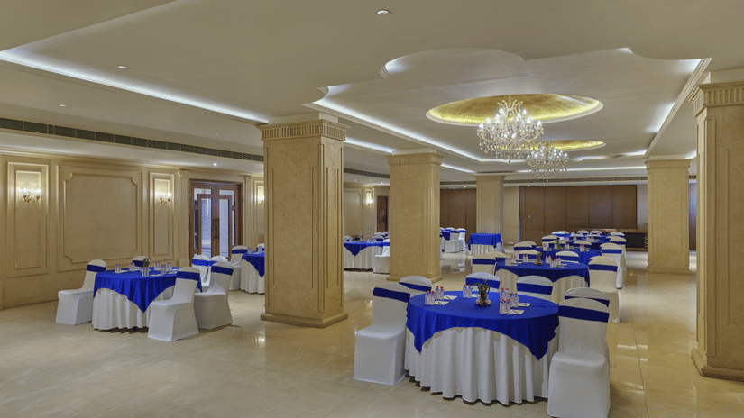 Spacious banquet hall with blue and white round table setups - Pride Elite Gandhinagar