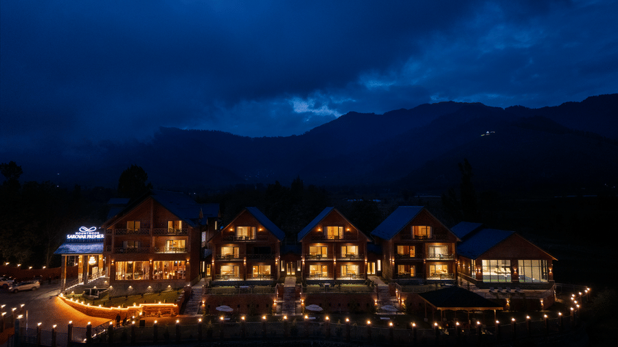 Night-time exterior of Mountnoor Sarovar Premiere, Pahalgam with warmly lit cottages overlooking the mountains.